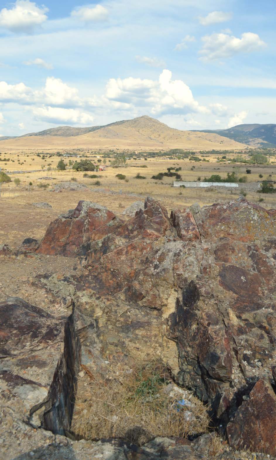 Figura 2. En primer plano, el pozo cegado de la mina de El Mojón. Al fondo, la característica silueta del cerro de La Atalaya, seguido a su izquierda por el cerro de Las Cardosillas y, más allá, por el cerro de Las Asperillas o cerro de La Abierta.